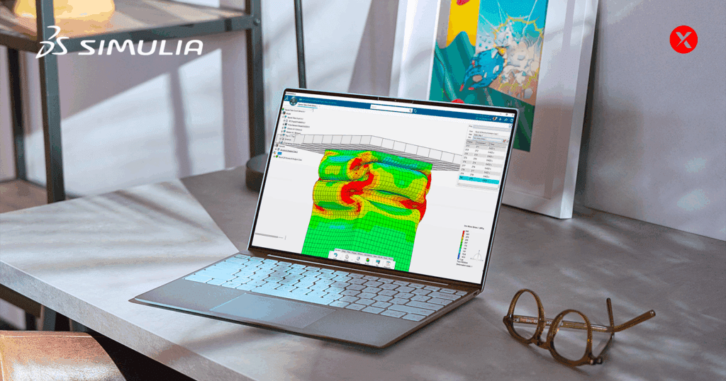 A laptop on a desk displays SIMULIA software running a finite element analysis of a rubber component under compression. The mesh is shown with a color contour plot of stress distribution in green, yellow, and red. The SIMULIA logo appears in the top left corner, with glasses placed on the desk beside the laptop.